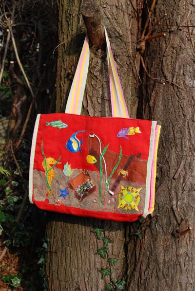 A bright red shopping type bag is displayed on a tree. The bag has fish on it swimming around a treasure chest.
